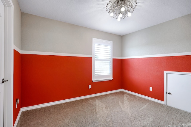 spare room with a textured ceiling, a notable chandelier, and carpet flooring