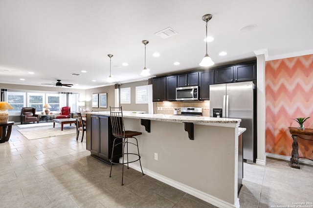 kitchen with hanging light fixtures, stainless steel appliances, a center island with sink, a breakfast bar, and light stone counters