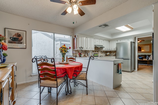 kitchen featuring kitchen peninsula, stainless steel fridge, light tile patterned floors, white cabinetry, and a textured ceiling