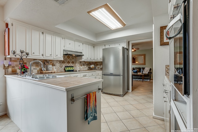 kitchen with tile countertops, kitchen peninsula, white cabinetry, and stainless steel refrigerator