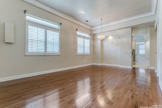 empty room with hardwood / wood-style flooring, crown molding, and a chandelier