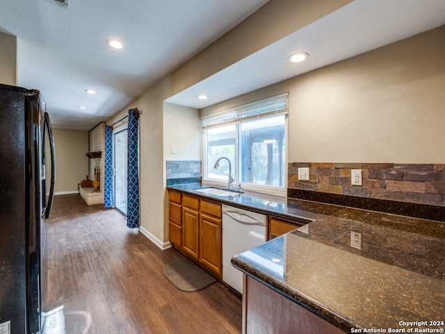 kitchen with backsplash, dark hardwood / wood-style flooring, black fridge, white dishwasher, and sink