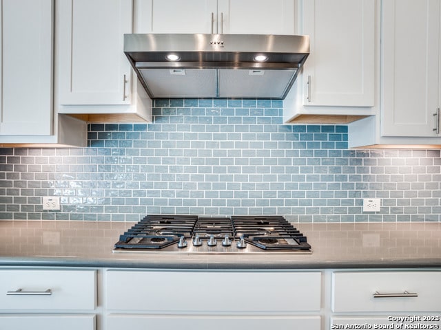 kitchen with ventilation hood, white cabinets, and backsplash