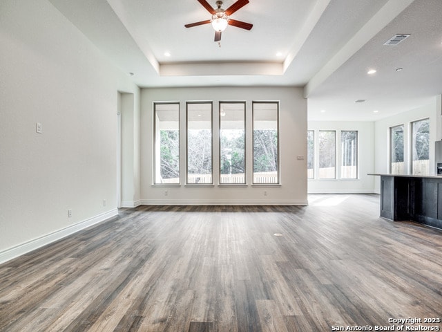 unfurnished living room featuring hardwood / wood-style flooring, a tray ceiling, and ceiling fan