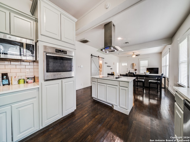 kitchen featuring a barn door, island range hood, backsplash, stainless steel appliances, and dark wood-type flooring