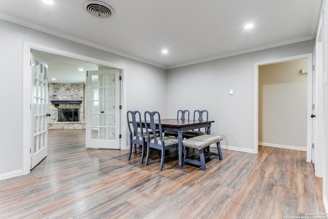 dining space with a stone fireplace, crown molding, hardwood / wood-style floors, and french doors