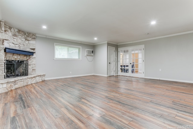 unfurnished living room featuring crown molding, a stone fireplace, a wall mounted air conditioner, and light hardwood / wood-style floors