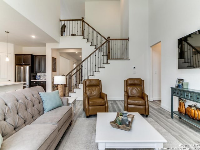 living area with stairway, a towering ceiling, light wood-style flooring, baseboards, and recessed lighting