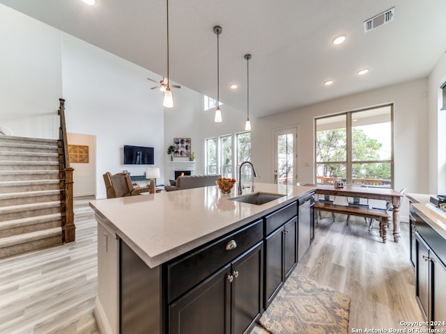 kitchen with light hardwood / wood-style flooring, a center island with sink, sink, decorative light fixtures, and ceiling fan