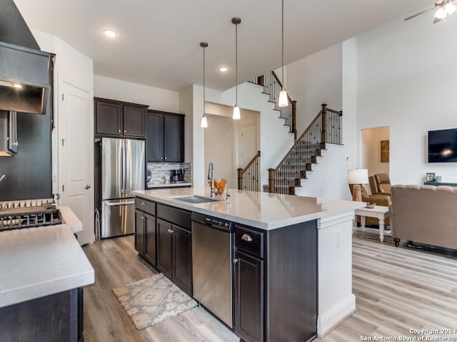 kitchen with a sink, stainless steel appliances, open floor plan, light wood-type flooring, and tasteful backsplash