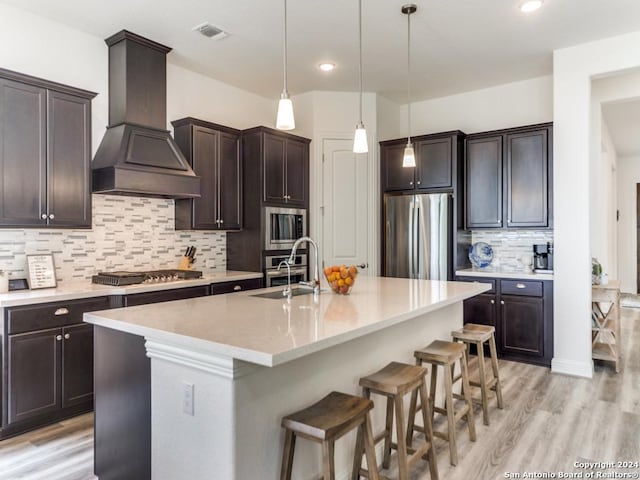 kitchen featuring stainless steel appliances, a sink, premium range hood, a kitchen bar, and dark brown cabinetry