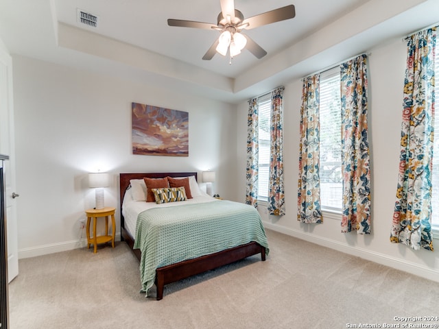 bedroom featuring ceiling fan, a raised ceiling, and light colored carpet