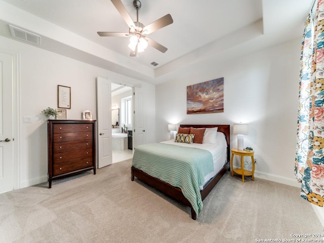 bedroom with light colored carpet, a tray ceiling, baseboards, and ensuite bath