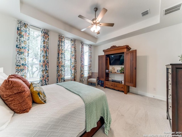 bedroom with light carpet, a raised ceiling, baseboards, and ceiling fan