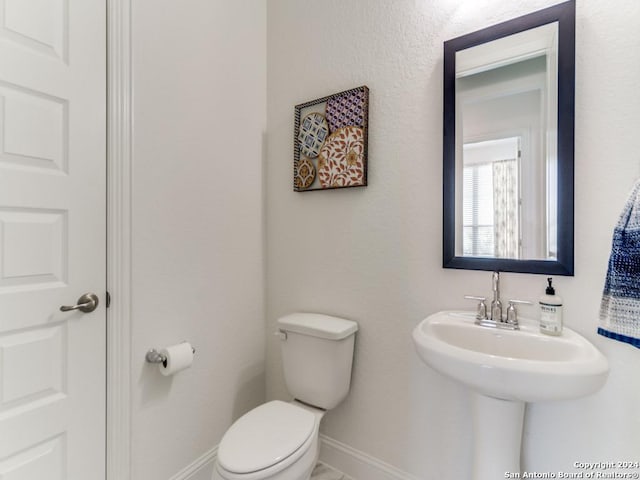 half bathroom with baseboards, toilet, and a sink