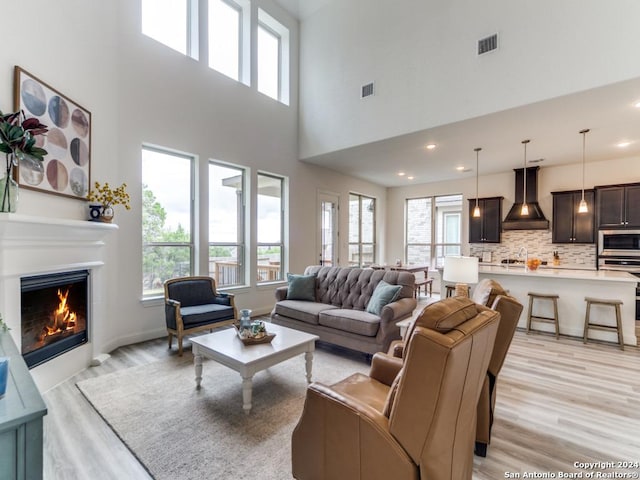 living room featuring healthy amount of natural light, light wood finished floors, a high ceiling, a glass covered fireplace, and recessed lighting