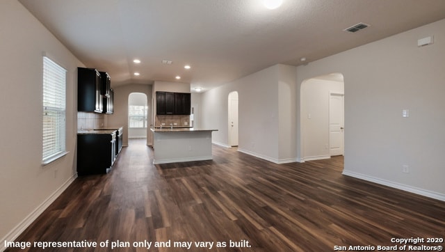 kitchen featuring dark wood-type flooring, backsplash, and an island with sink