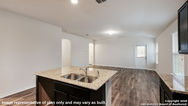 kitchen with dark hardwood / wood-style floors, a center island with sink, sink, vaulted ceiling, and light stone counters