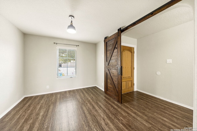 unfurnished room with dark hardwood / wood-style floors, a textured ceiling, and a barn door