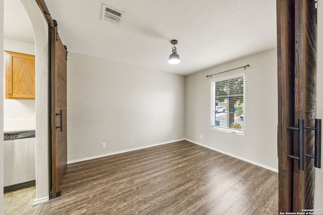 spare room with a textured ceiling, a barn door, and dark hardwood / wood-style flooring