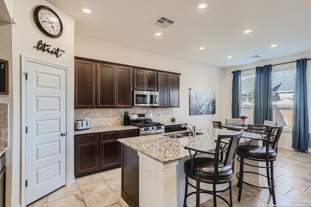 kitchen featuring a breakfast bar area, stainless steel appliances, a center island with sink, sink, and light stone countertops