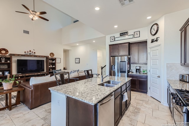 kitchen with appliances with stainless steel finishes, a kitchen island with sink, light stone countertops, and a high ceiling