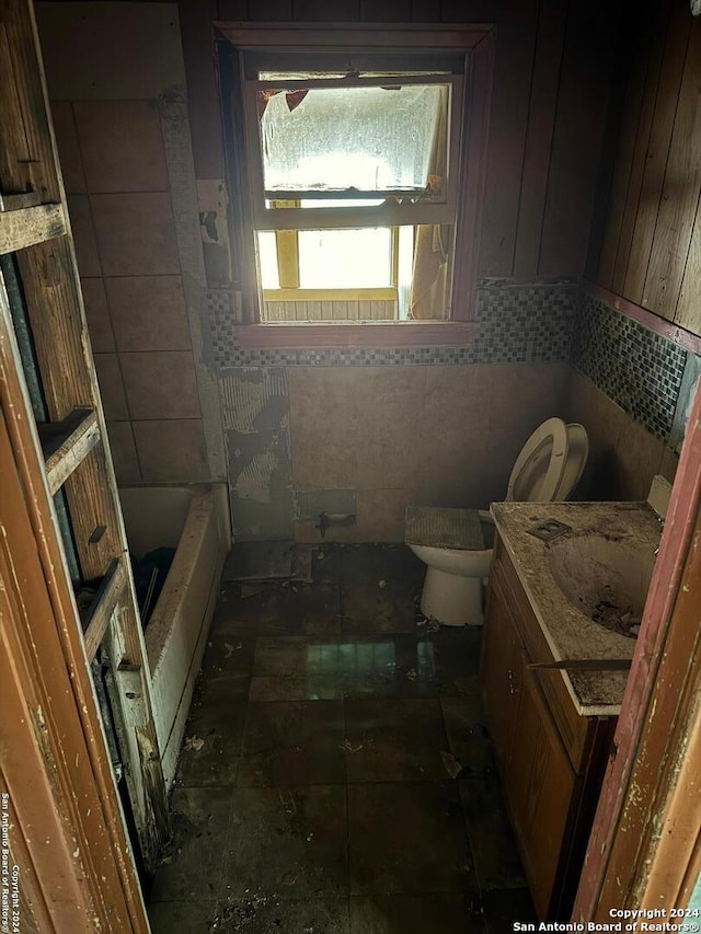 bathroom featuring vanity, a tub, toilet, and tile walls