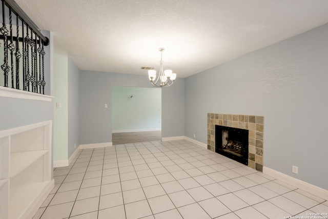 unfurnished living room with an inviting chandelier, a textured ceiling, a tile fireplace, and light tile patterned floors