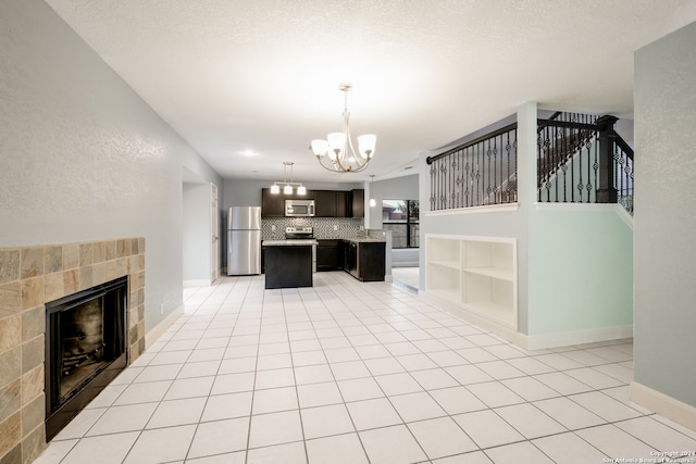 kitchen featuring appliances with stainless steel finishes, dark brown cabinets, a center island, a tiled fireplace, and an inviting chandelier