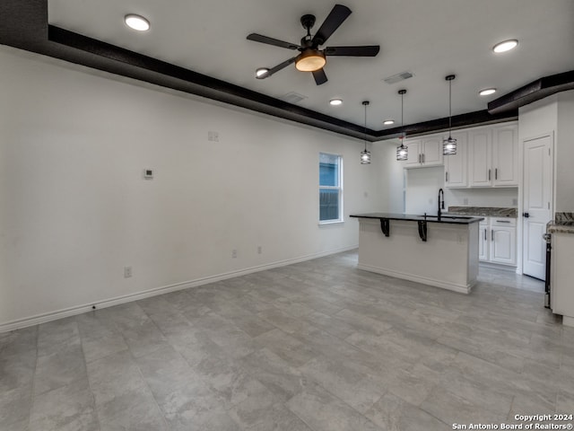 kitchen with white cabinets, ceiling fan, a tray ceiling, sink, and decorative light fixtures