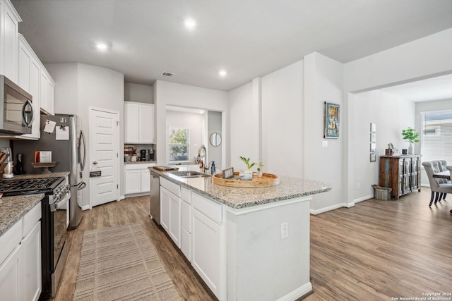 kitchen with appliances with stainless steel finishes, white cabinets, a kitchen island with sink, and hardwood / wood-style flooring