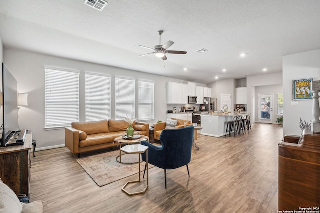 living room featuring light hardwood / wood-style floors, a textured ceiling, ceiling fan, and a wealth of natural light