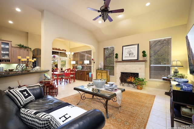 tiled living room with lofted ceiling, a stone fireplace, and ceiling fan with notable chandelier