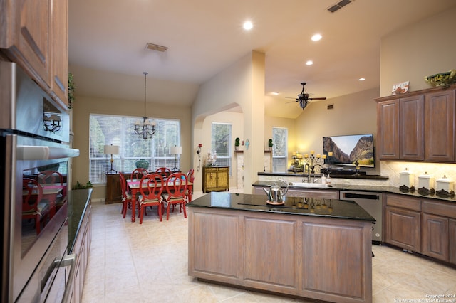 kitchen with lofted ceiling, dark stone countertops, a center island, appliances with stainless steel finishes, and ceiling fan with notable chandelier