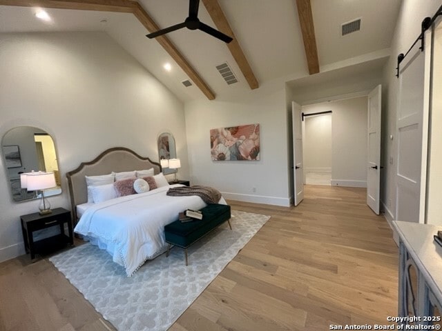 bedroom with a barn door, high vaulted ceiling, beam ceiling, and light hardwood / wood-style floors