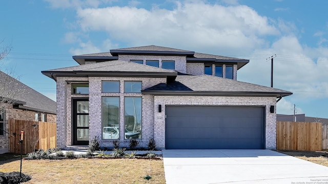 prairie-style house with an attached garage, roof with shingles, fence, and driveway