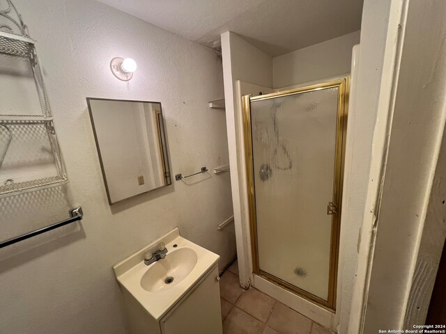 bathroom featuring a shower with door, vanity, a textured ceiling, and tile patterned flooring