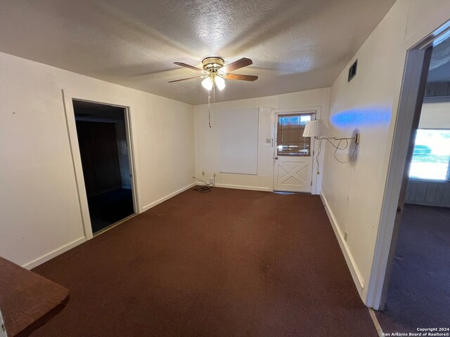 unfurnished room featuring a wealth of natural light, dark carpet, a textured ceiling, and ceiling fan