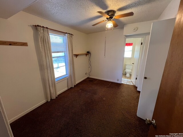 unfurnished room featuring a wealth of natural light, a textured ceiling, dark carpet, and ceiling fan