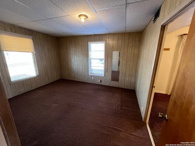 carpeted empty room with a paneled ceiling and wooden walls