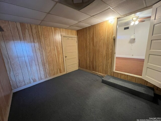 basement with ceiling fan, wood walls, carpet floors, and a drop ceiling