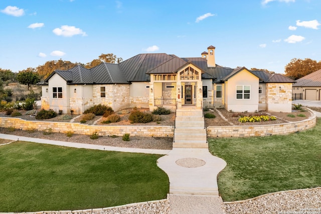 modern farmhouse style home with a standing seam roof, stone siding, a front lawn, and metal roof