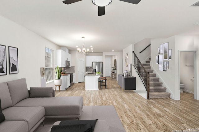 living room with sink, light wood-type flooring, and ceiling fan with notable chandelier