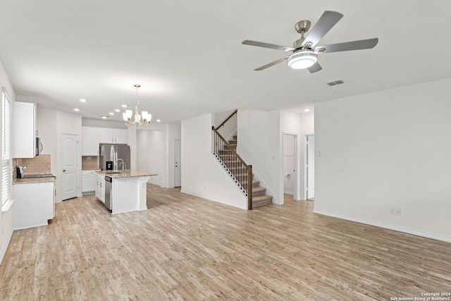 kitchen with tasteful backsplash, light wood-type flooring, hanging light fixtures, stainless steel appliances, and a center island with sink