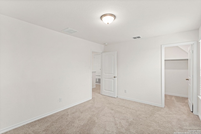 unfurnished bedroom with a closet, light carpet, and a walk in closet