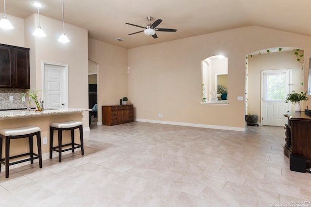 kitchen with a breakfast bar area, backsplash, light stone countertops, pendant lighting, and ceiling fan