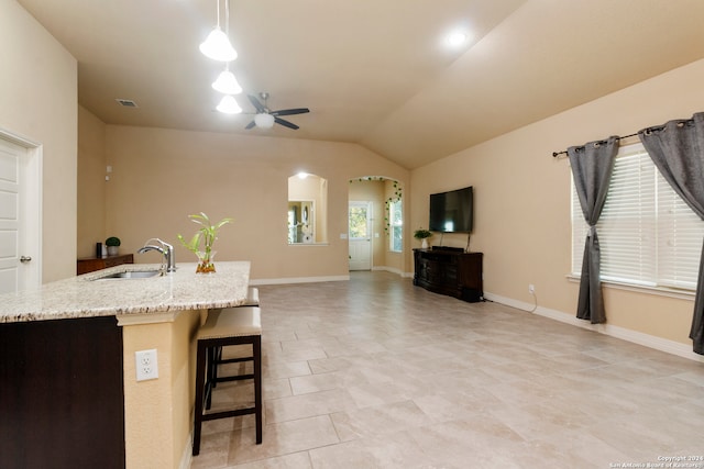 kitchen featuring lofted ceiling, ceiling fan, a kitchen bar, sink, and decorative light fixtures