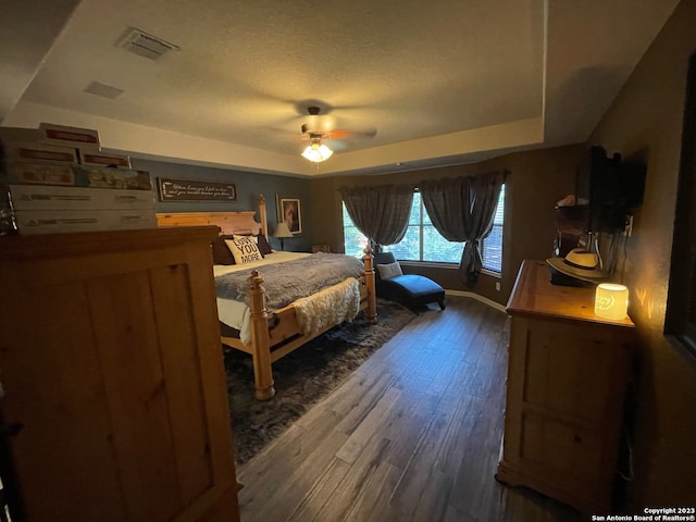 bedroom featuring a textured ceiling, dark wood-type flooring, a raised ceiling, and ceiling fan