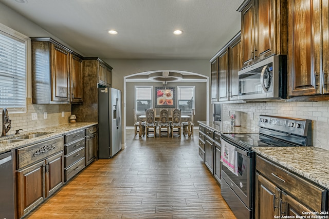 kitchen with dark brown cabinets, backsplash, light wood-type flooring, sink, and stainless steel appliances