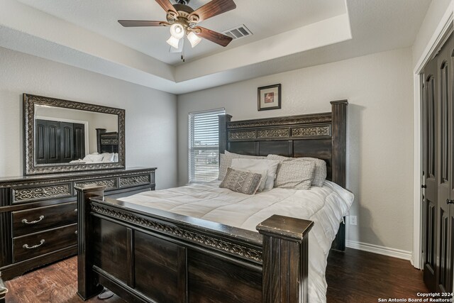 bedroom with a closet, ceiling fan, a raised ceiling, and dark hardwood / wood-style flooring